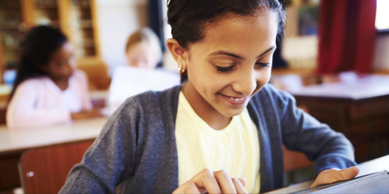 Elementary aged student reading a book while sitting at a desk.