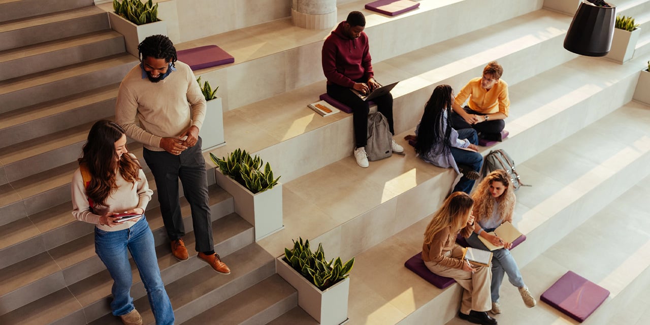 College students sitting on stairs inside of an academic building.