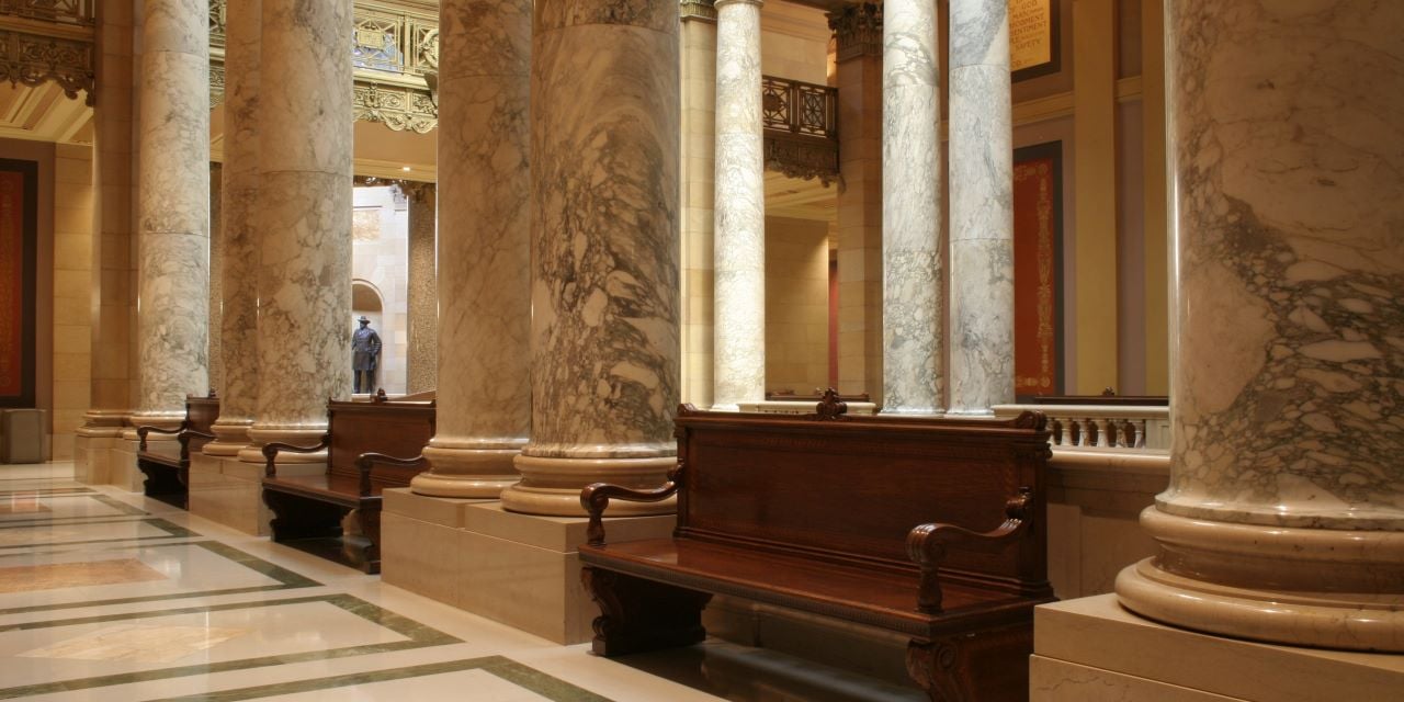 Interior view of a government building with wood benches and marble columns.