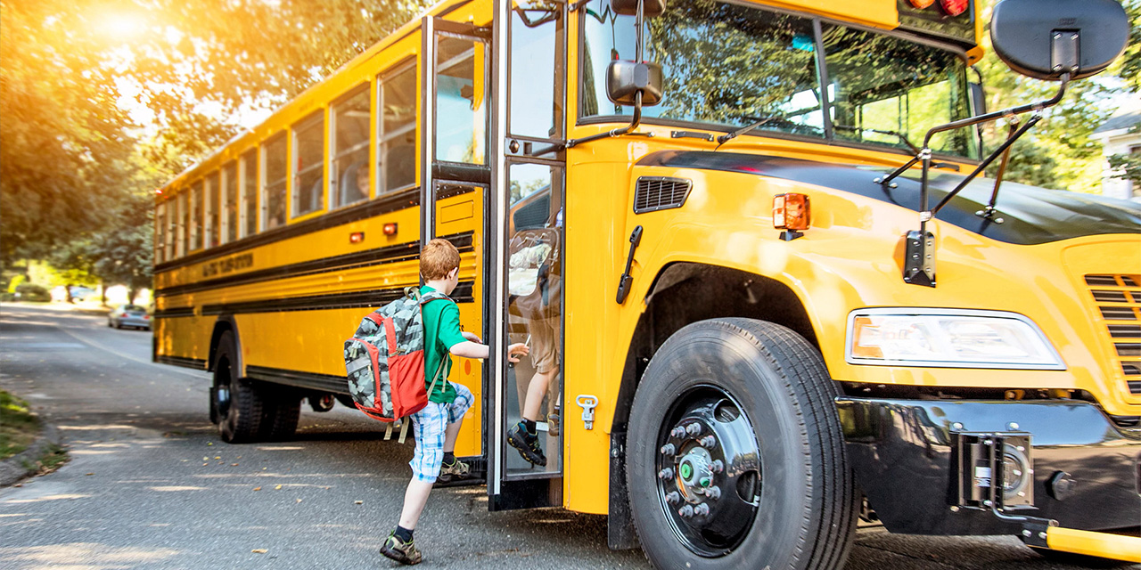 Elementary school aged child getting onto a school bus.