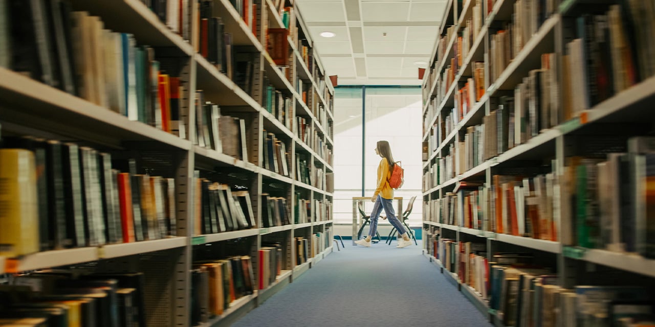 Student walking past two rows of books in a library.
