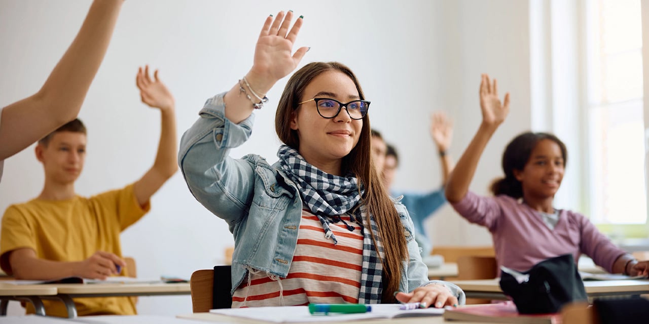 Middle school ages students raising their hands while sitting in class.