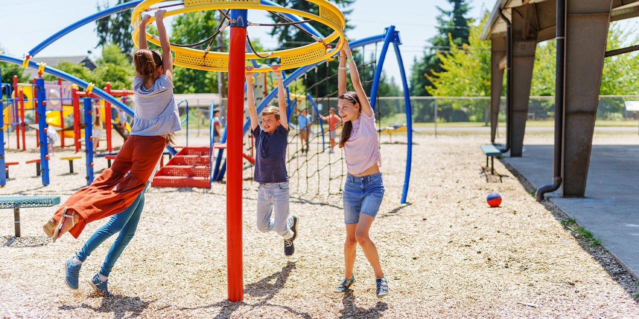 Children hanging on playground equipment in a park during the day.