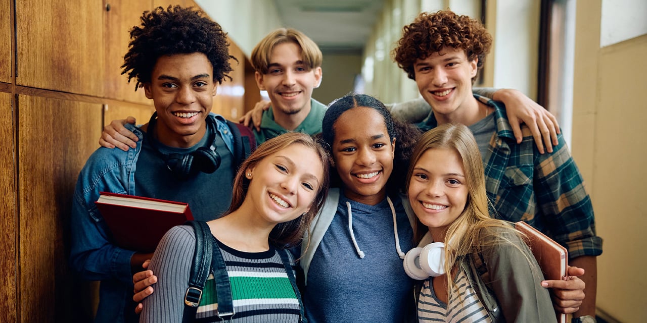 Group of high school students standing in a school hallway with arms around shoulders.
