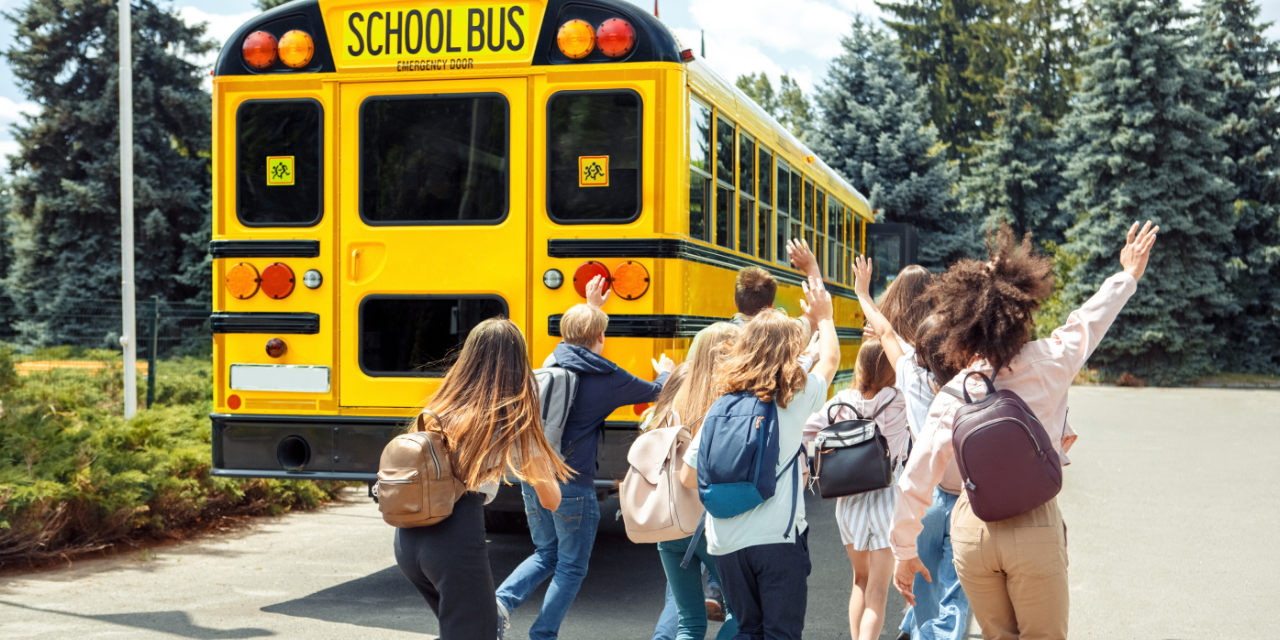 Elementary aged school children running toward a school bus.