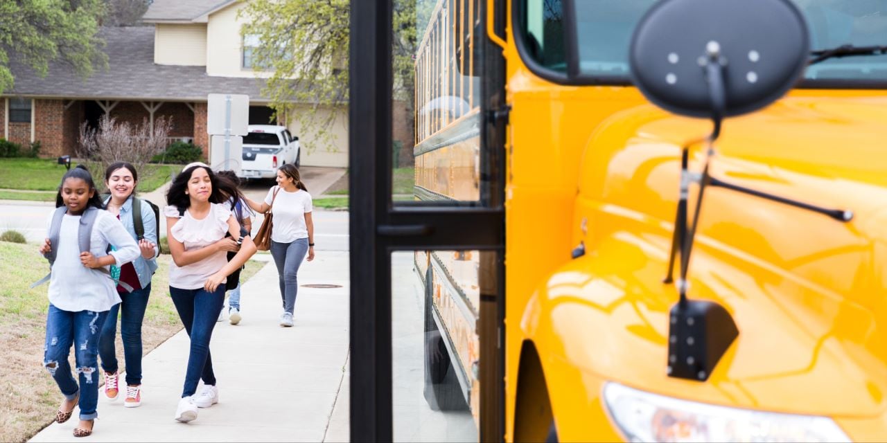 Middle school aged children walking in a line toward a school bus.