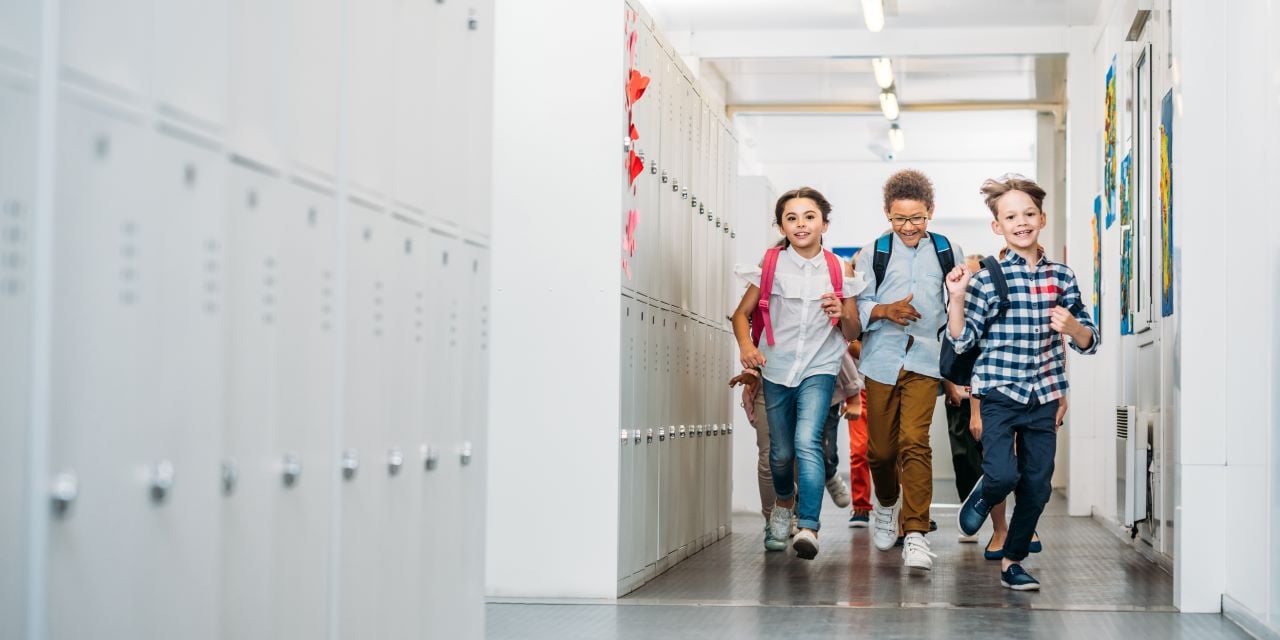 Children smiling and running down a school hallway.