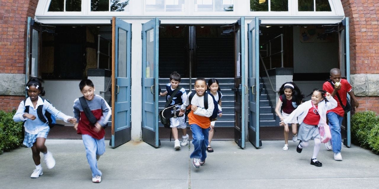 Kids smiling and laughing while exiting doors of a school.