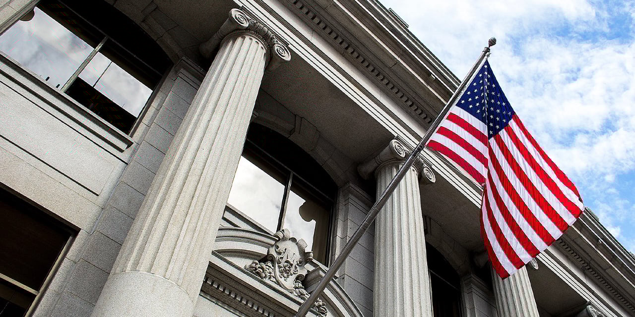 Outside view of a building with stone pillars and an American flag.