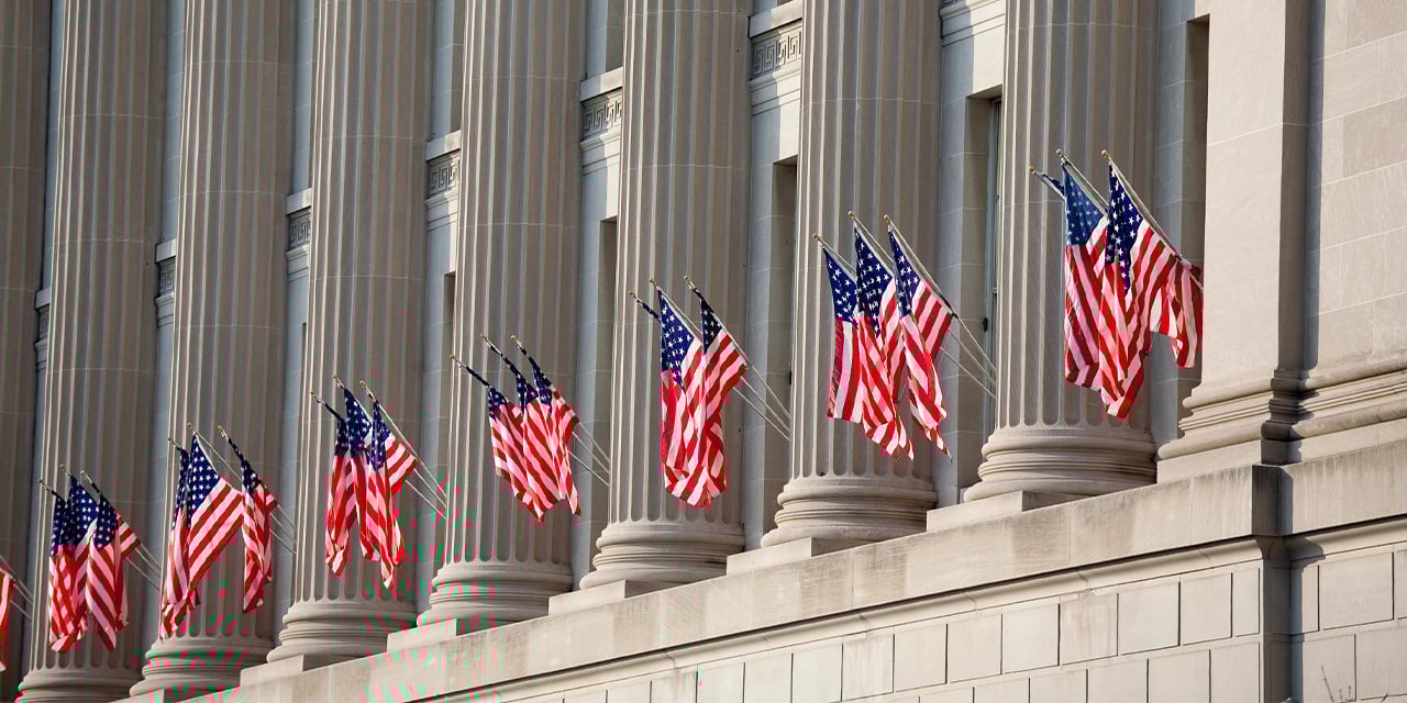 Exterior view of a building with stone pillars and American flags flying between the pillars.