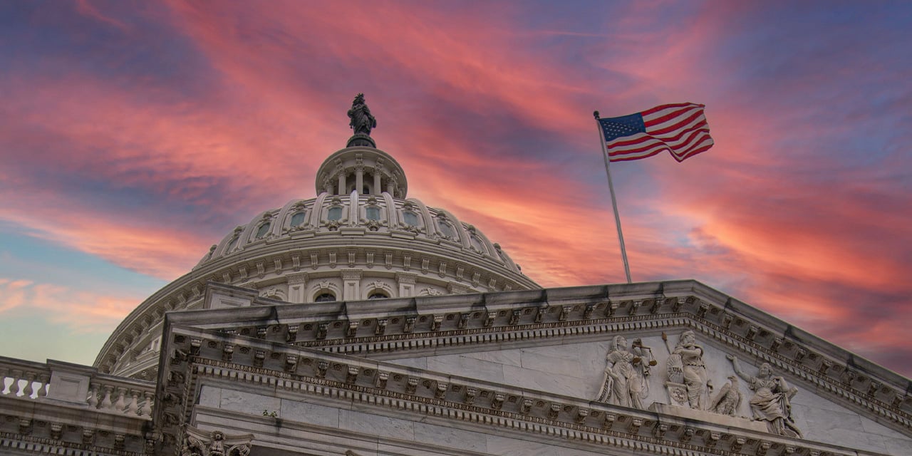 U.S. Capitol building dome and American flag at sunset with dramatic pink and orange clouds.
