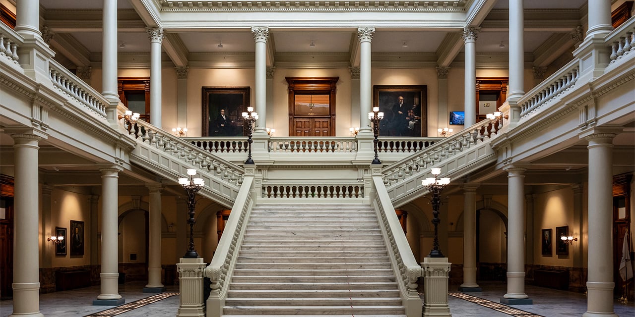 Large stone staircase inside of an ornate building with stone pillars.