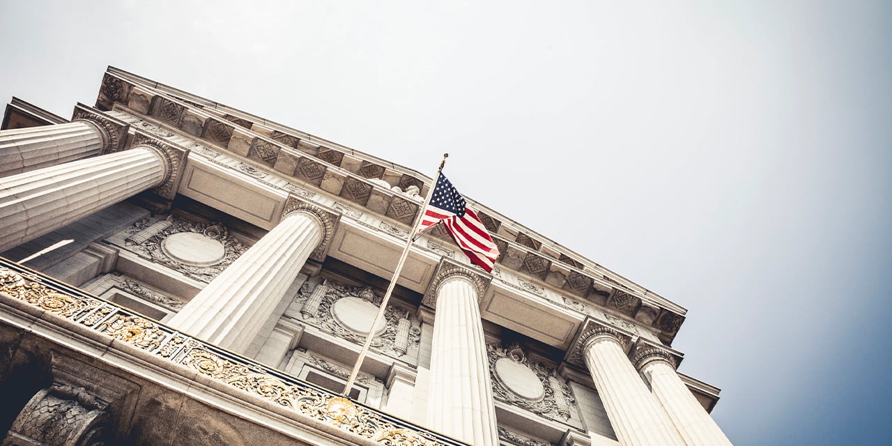 Exterior view looking up at a municipal building with stone pillars and an American flag.