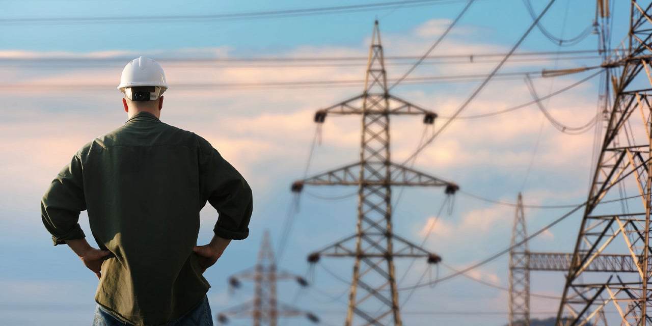 Man wearing a hardhat looking out at power lines during the day.