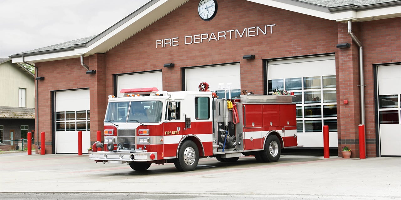Firetruck parked outside of a brick fire station. 
