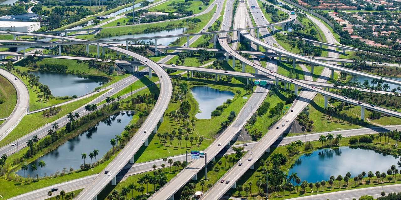 Aerial view of a large highway interchange with curving overpasses, green landscape, and small lakes.