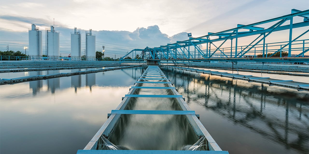Water treatment basin with metal walkways and flowing channels beneath a large blue structural frame at sunset.
