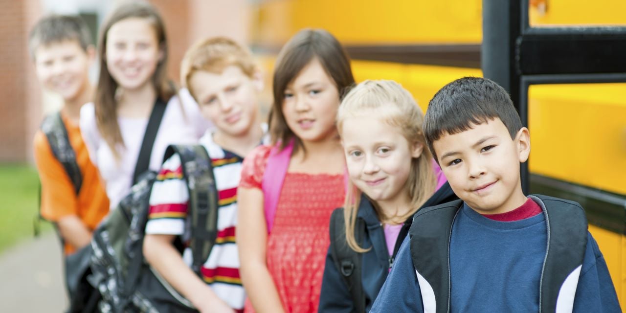Elementary aged students standing in line outside of a bus.