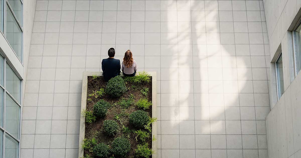 Two people sitting on the edge of a planter inside an office building.
