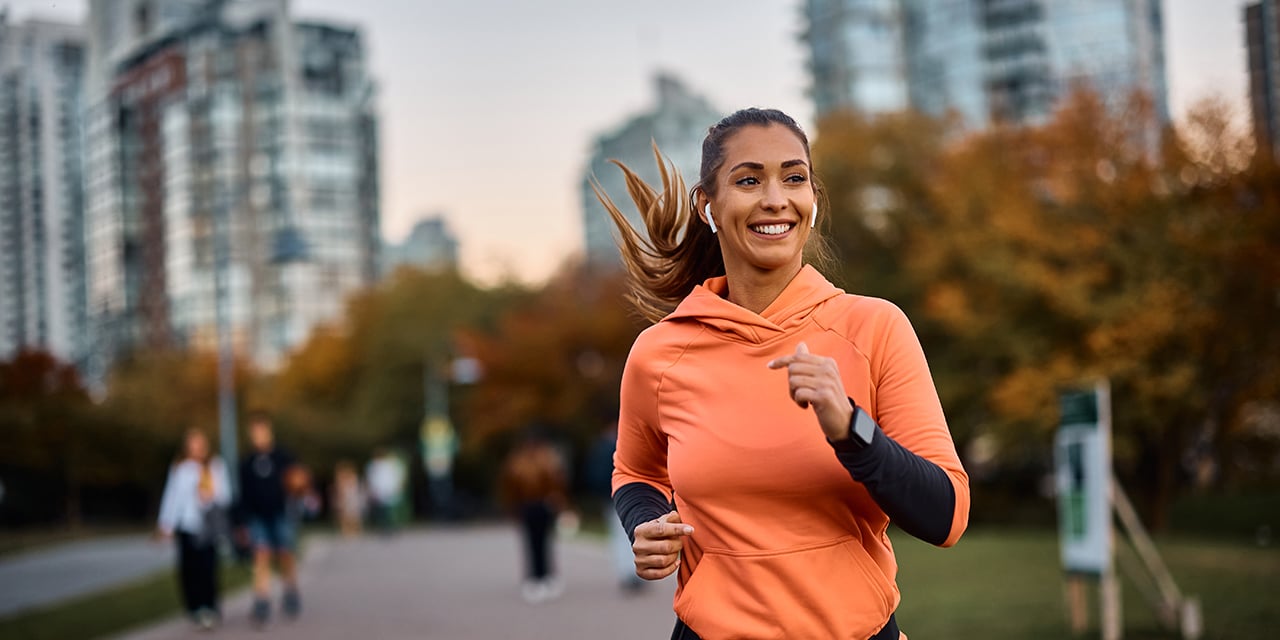 Woman running on a path in a park in a city earing headphones.