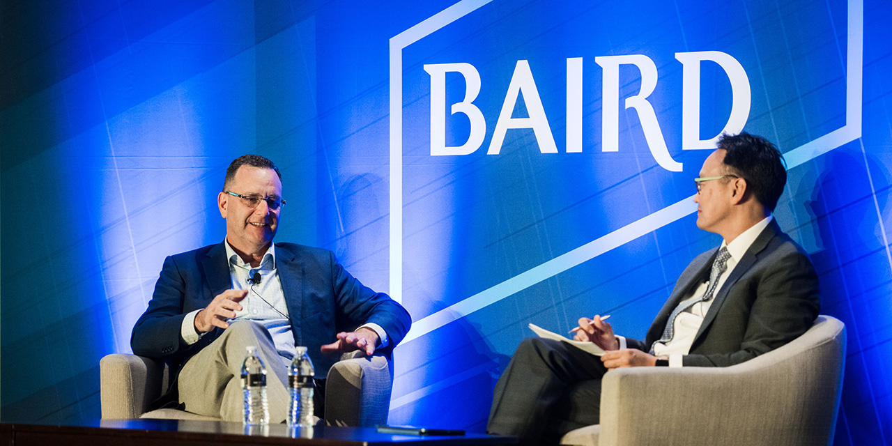 Two men on stage in front of a Baird logo during a pane discussion.